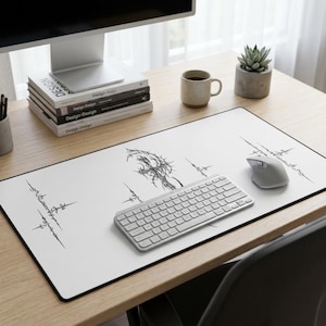 May include: White rectangular desk mat with a black border, featuring a black abstract design. A wireless keyboard and mouse are on the mat. The mat is on a wooden desk with a computer monitor, books, and a coffee mug.