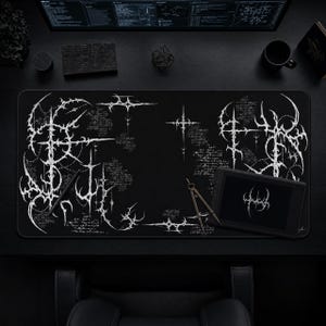 May include: A rectangular black desk mat featuring an intricate white graphic design composed of sharp, angular, thorn-like lines and abstract calligraphic script. The pattern is distributed across the left and right sides, leaving the centre clear.