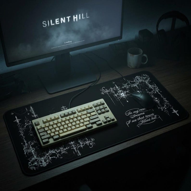 K&ouml;nnte beinhalten: Eine schwarze Gaming-Mausunterlage mit wei&szlig;em Grafikdesign und dem Text "In my restless dreams I see that town Silent Hill." Eine beige Tastatur und eine schwarze Maus befinden sich auf dem Pad. Ein Computermonitor zeigt "SILENT HILL".