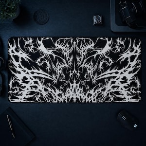 May include: A rectangular desk mat featuring a high-contrast black and white design. The surface is covered in an intricate, symmetrical pattern of sharp, jagged, and flowing lines that resemble organic, thorny, or metallic web-like structures.
