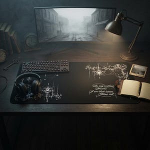 K&ouml;nnte beinhalten: Schwarzes Gaming-Mauspad mit wei&szlig;en grafischen Designs und dem Text "In my restless dreams I see that town Silent hill." Auf dem Schreibtisch befinden sich eine Tastatur, Kopfh&ouml;rer und eine Schreibtischlampe. Ein Computermonitor zeigt eine neblige Stra&szlig;enszene.