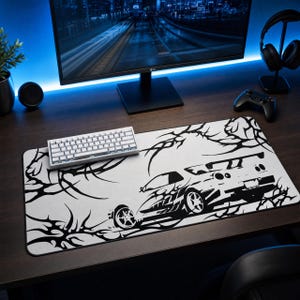 May include: A rectangular desk mat featuring a high-contrast black and white graphic design. The print displays a stylized sports car viewed from the rear quarter angle, surrounded by intricate, sharp, thorn-like tribal patterns.