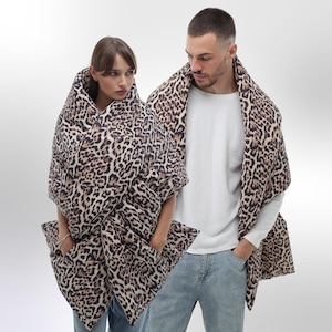 May include: Two people wearing a brown and black leopard print blanket as a jacket. The blanket is made of a soft, quilted fabric.