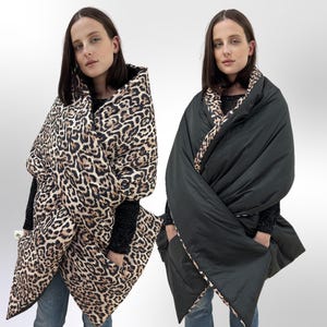 May include: A reversible oversized blanket scarf with a leopard print on one side and a solid black colour on the other side. The scarf has pockets on both sides.