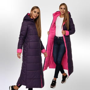 May include: A long, purple puffer coat with a pink lining and a hood. The coat has a zip closure and a quilted design.