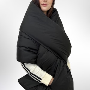 May include: A black puffer scarf with a unique design. The scarf is worn around the neck and shoulders, and it has a large, puffy shape.
