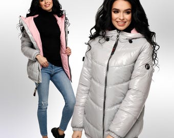 Pode incluir: Uma jaqueta puffer reversível com exterior prateado e interior rosa. A jaqueta tem fecho de correr, capuz e um logotipo na manga.