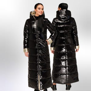 May include: A long black puffer coat with a shiny finish and gold accents. The coat has a hood and a zip closure.