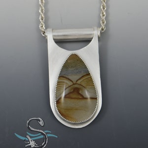 May include: A silver pendant necklace with a teardrop-shaped stone set in a silver bezel. The stone is a light brown with darker brown and gray swirls. The pendant hangs from a silver chain.