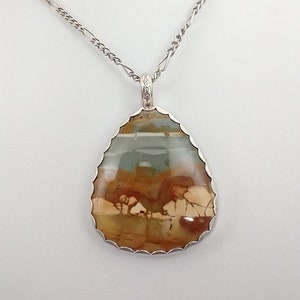 May include: A teardrop-shaped pendant necklace with a silver chain. The pendant features a large, polished stone with a mix of brown, beige, and blue-green colors. The stone is set in a silver bezel with a scalloped edge, creating a unique jewelry piece.