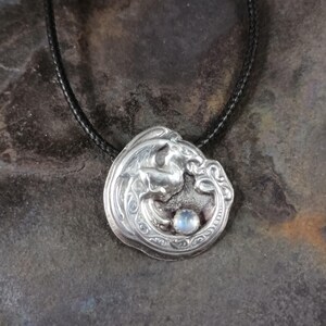 May include: A silver pendant necklace with a dragon design and a moonstone. The dragon is curled around the moonstone, which is set in the center of the pendant. The pendant is on a black cord.