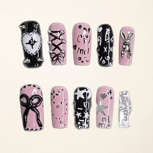 May include: A set of ten artificial nails in various designs. The nails feature a mix of black and pink colors with decorative elements such as bows, stars, and a bunny. The text "DreamDimensionsHK" is written in pink cursive at the top.