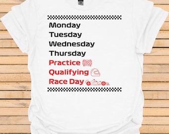 Puede incluir: Camiseta blanca con un borde de cuadros negros y blancos. El texto "Lunes, Martes, Miércoles, Jueves, Práctica, Clasificación, Día de carrera" está impreso en rojo. Un mando de videojuegos, un casco y un coche de carreras también están impresos en rojo.