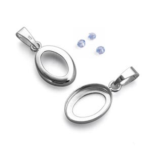 May include: Two silver oval pendant settings with a loop for a chain. Three small, light blue gemstones are scattered nearby. The pendants have a polished finish against a white background.