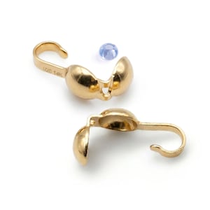 Könnte beinhalten: Zwei goldfarbene Schmuckverschlüsse mit Haken und einem abgerundeten, scharnierartigen Design. Die Verschlüsse befinden sich neben einem kleinen, hellblauen Edelstein. Auf einem Verschluss steht "1/20 14K".