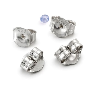 May include: A collection of silver earring backs and a single blue bead on a white background. The earring backs are stamped with "925". The earring backs are in various shapes and sizes.