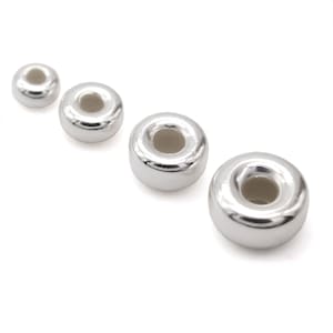 May include: Four shiny, silver-coloured donut-shaped beads are arranged diagonally on a white background. The beads have a smooth, reflective surface and a hole in the centre. The beads vary slightly in size.