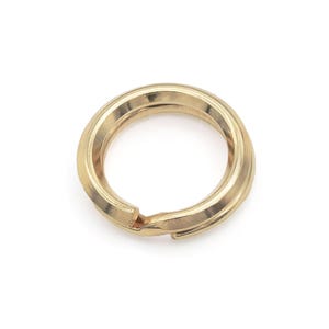 Puede incluir: Un llavero de metal de color dorado con una superficie lisa y redondeada.