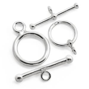 Puede incluir: Tres cierres de metal plateados para la elaboración de joyas. Los cierres son un cierre de palanca, un cierre de langosta y un cierre de anillo.