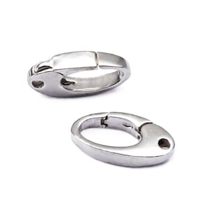 May include: Two silver-toned metal oval-shaped clasps for jewellery making. The clasps are open and ready to be attached to a necklace or bracelet.