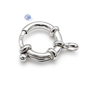 May include: A circular silver spring ring clasp featuring a polished finish and a small attached loop. The metal surface is stamped with the number 925, indicating sterling silver composition. A small, light blue bead is positioned nearby.