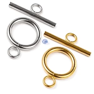 May include: Two toggle clasps for jewellery making, one in a silver tone and one in a gold tone. Each set consists of a circular ring with a small loop and a matching bar component with a central loop. A single small light blue bead is placed between them.