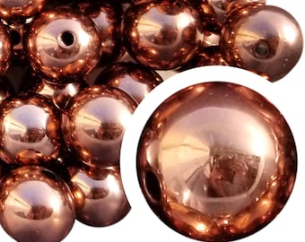 May include: A collection of shiny, copper-colored, spherical beads. Each bead has a smooth, reflective surface and a small hole drilled through it. The beads are clustered together, with a close-up view of a single bead in the lower right corner.