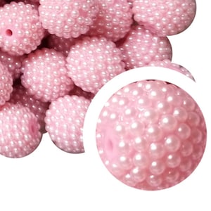 May include: A close-up of a pile of pink pearl beads. The beads are round and have a textured surface. They are perfect for making jewelry or other crafts.