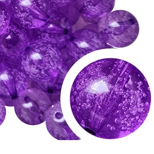 May include: A collection of translucent purple beads with a glossy finish. The beads have a spherical shape and are clustered together. Each bead has a small hole for stringing. A close-up shows the internal texture and bubbles within the beads.