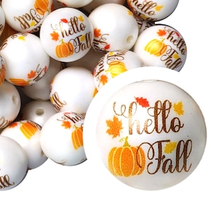 May include: White round beads with a gold "Hello Fall" design and a pumpkin graphic. The beads are scattered on a white surface.