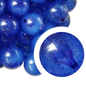 May include: A close-up of a pile of blue glass beads with a textured surface. The beads are round and have a shiny finish.