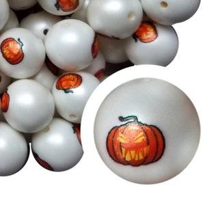 May include: A close-up of white round beads with orange and black jack-o'-lantern faces printed on them. The beads are ideal for making Halloween jewellery or crafts.