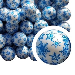 May include: A group of white, round, plastic beads with a blue snowflake pattern. The beads are approximately 1 inch in diameter.
