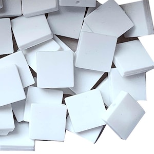 May include: A collection of small, square, white tiles. The tiles are scattered, with some overlapping. The edges of the tiles are slightly rounded, and they have a smooth, matte finish. The image is well-lit, and the tiles appear clean and new.