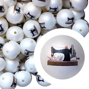 May include: White round beads with a sewing machine design. The beads have a glossy finish and a small hole for stringing. The sewing machine illustration is black, red, and brown. These beads are suitable for jewelry making and craft projects.