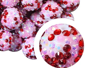 Op de afbeelding: Roze en rode ronde kralen met een glinsterende afwerking. De kralen zijn bedekt met kleine rode strass steentjes.