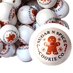 May include: White wooden beads with the text "Sugar N Spice Cookie Co." and a gingerbread man graphic in brown and red. The beads are round with a hole for stringing.