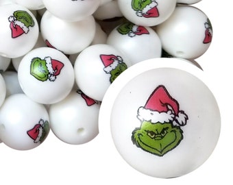 Könnte beinhalten: Weiße, runde Perlen mit einem Cartoon-Bild einer grünen Figur mit roter Weihnachtsmütze. Die Perlen eignen sich für Bastelarbeiten und die Schmuckherstellung. Die Grinch-Themenperlen sind eine festliche Ergänzung für Urlaubsprojekte.
