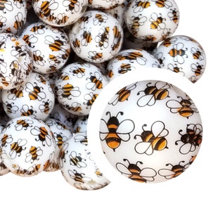 May include: White round beads with a repeating pattern of cartoon bees in black and orange. The beads are clustered together, with a close-up view of a single bead showing the bee design in detail. These beads are suitable for jewelry making and crafts.