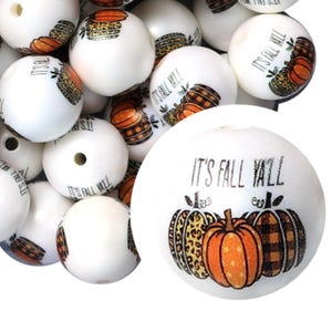 May include: White wooden beads with a fall theme. The beads are decorated with pumpkins in various patterns, including leopard print and plaid. The text "It's Fall Y'all" is printed on the beads.