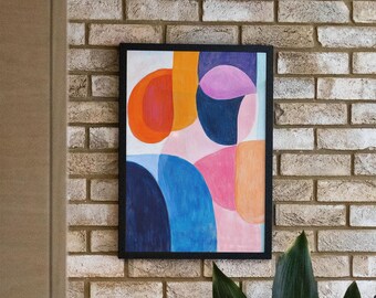 May include: A framed abstract painting with a black frame. The painting features a colorful design of overlapping circles and arcs in shades of orange, pink, blue, and black. The painting is hanging on a brick wall.