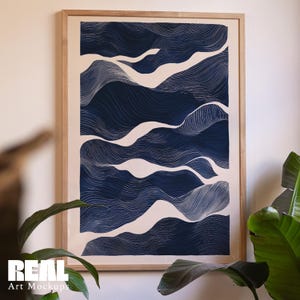 May include: Framed art print featuring an abstract design of navy blue and white wavy lines, resembling a landscape or water pattern. The artwork is displayed in a natural wood frame, adding a touch of warmth. The print is a Real Art Mockups product.