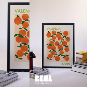 May include: Two framed prints of orange trees with the text "Valencia, Spain" on a white background. The prints are on a white surface with books and a lamp.