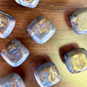 May include: Ten small, square, decorative ceramic tiles with a marbled pattern in shades of brown, blue, and gold. The tiles have a slightly raised, textured surface.