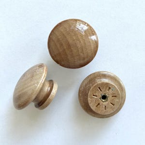 K&ouml;nnte beinhalten: Drei Holzkn&ouml;pfe mit nat&uuml;rlicher Oberfl&auml;che. Zwei Kn&ouml;pfe sind rund und einer hat einen kleinen Stiel. Die runden Kn&ouml;pfe haben eine leicht erh&ouml;hte Mitte.