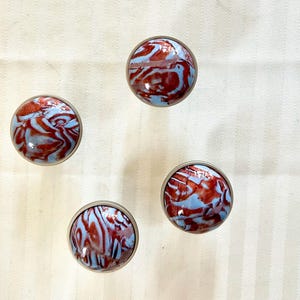 May include: Four round, decorative knobs with a silver metal base and a blue and red marbled design.
