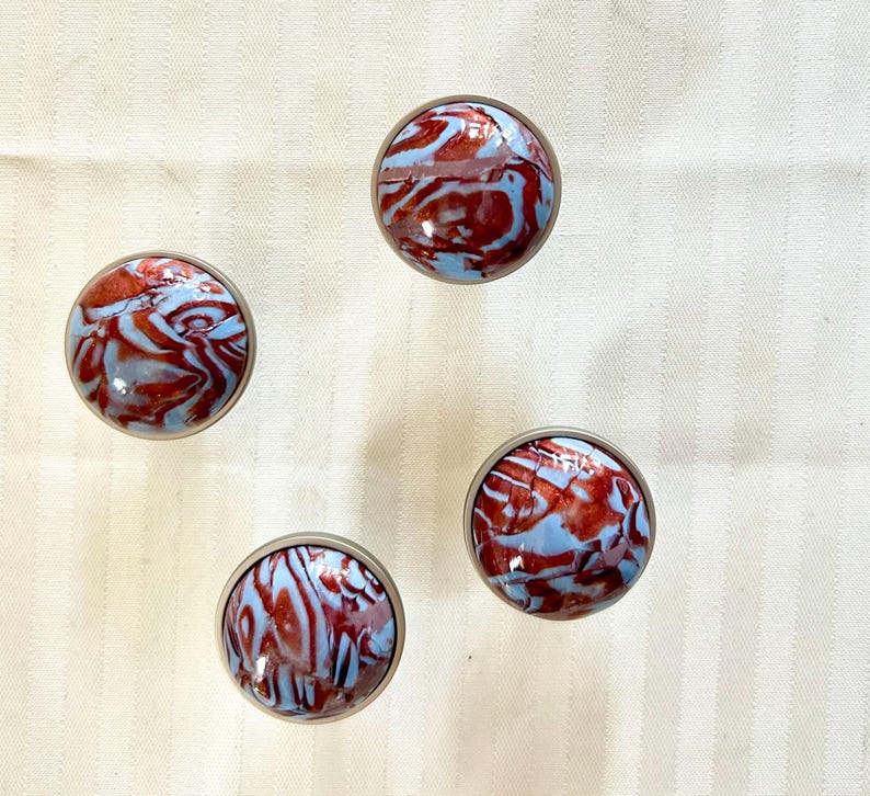 May include: Four round, decorative knobs with a silver metal base and a blue and red marbled design.