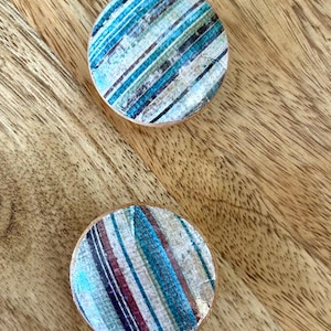 Pode incluir: Dois botões redondos de madeira com um padrão listrado azul, branco e marrom.