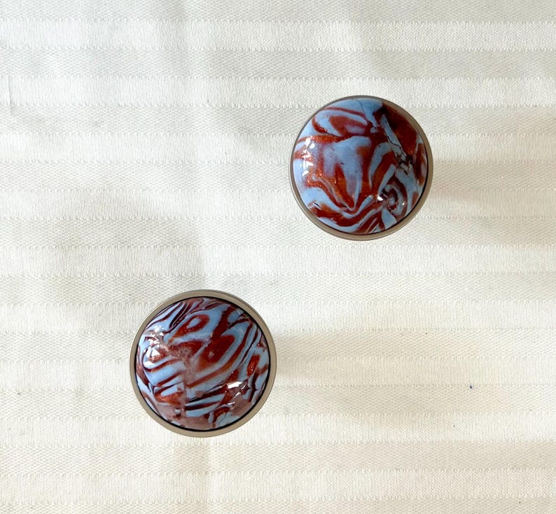 May include: Two round, silver-colored knobs with a blue and red marbled design.