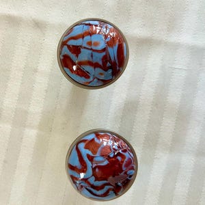 May include: Two round, blue and red marbled glass bottle stoppers. The stoppers have a shiny, iridescent finish.